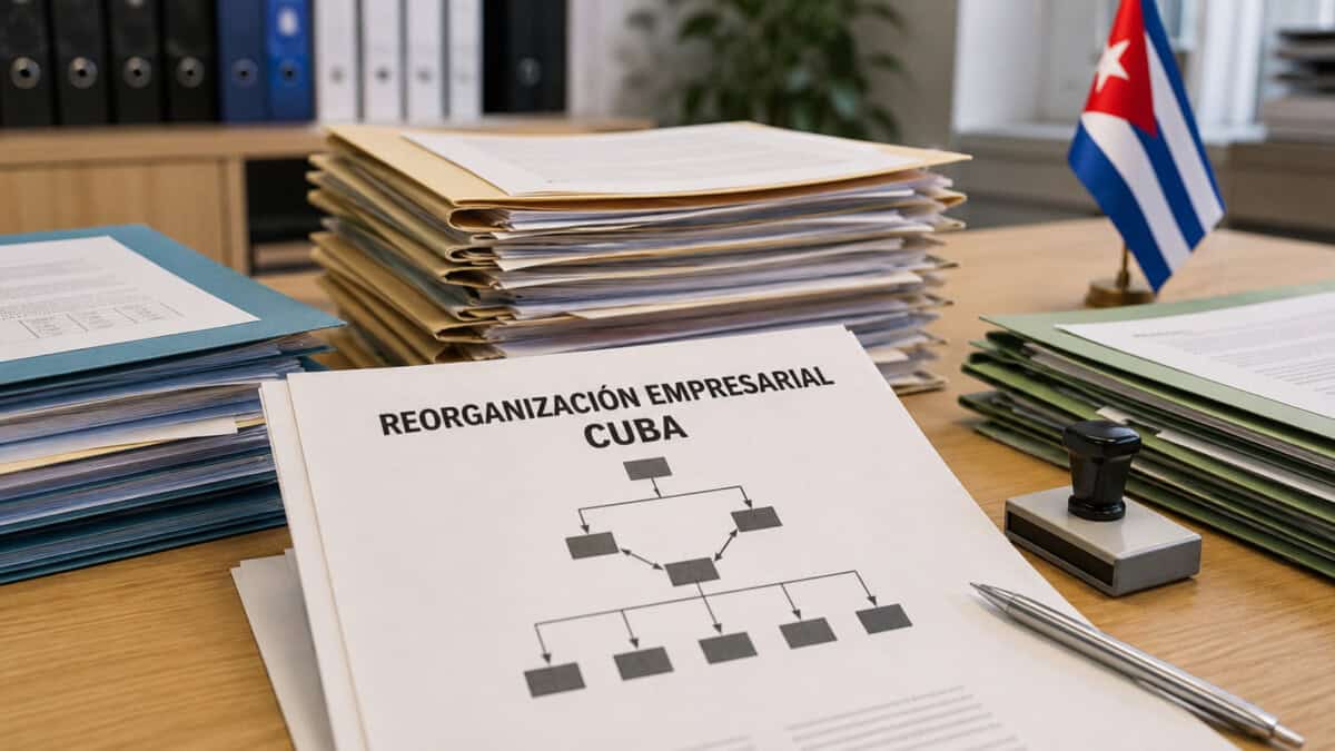Expedientes y documento sobre reorganización empresarial sobre una mesa de oficina, junto a una bandera cubana.