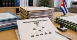 Expedientes y documento sobre reorganización empresarial sobre una mesa de oficina, junto a una bandera cubana.