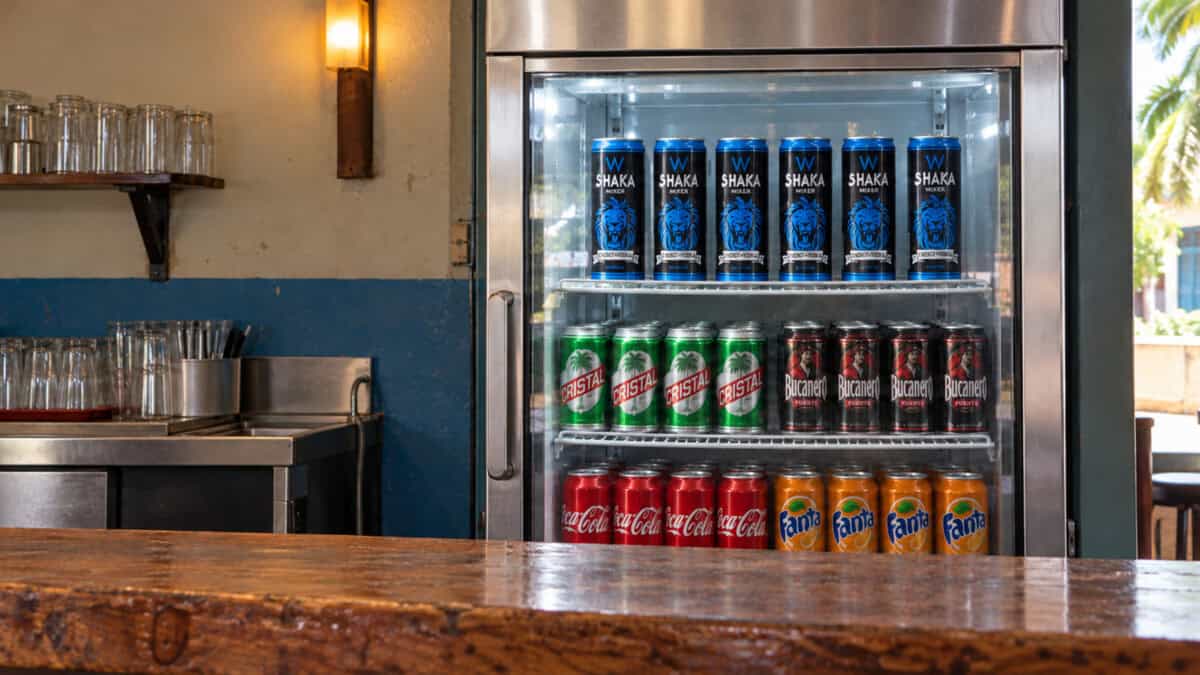 Seis latas de Shaka en un exhibidor con puerta de cristal, junto a cervezas Cristal, Bucanero y refrescos.