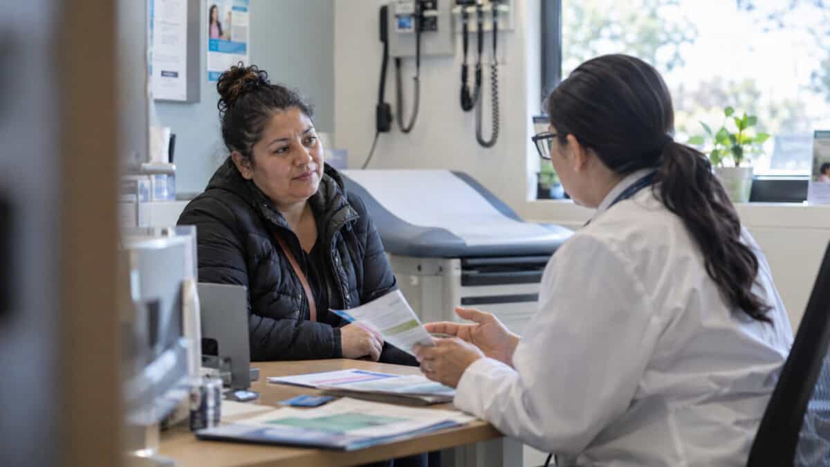 Inmigrante adulta conversa con una profesional sanitaria sobre atención médica y seguro de salud en una clínica de Estados Unidos.