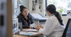 Inmigrante adulta conversa con una profesional sanitaria sobre atención médica y seguro de salud en una clínica de Estados Unidos.