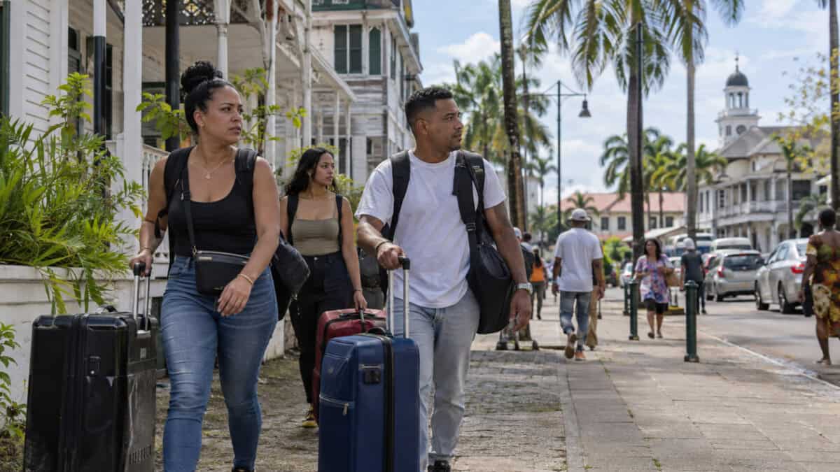 Tres viajeros con maletas caminan por una calle inspirada en Paramaribo, Surinam.