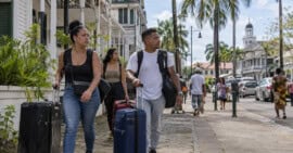 Tres viajeros con maletas caminan por una calle inspirada en Paramaribo, Surinam.