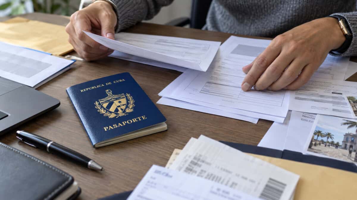Persona organiza formularios consulares junto a un pasaporte cubano cerrado.