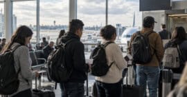 Grupo de adultos con equipaje de mano y documentos espera cerca de una puerta de embarque en un aeropuerto.