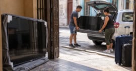 Dos adultos descargan un televisor Samsung junto a una vivienda en La Habana, mientras otro permanece protegido en la entrada.