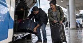 Dos adultos descargan maletas del compartimento de un autobús en una terminal de ómnibus de Uruguay.