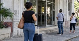 Mujer con una maleta espera frente a una oficina de trámites en Cuba.