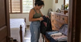 Mujer cubana guarda un pasaporte en su mochila junto a una maleta abierta en una habitación.