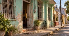 Fachada de una vivienda cubana con paredes desgastadas, ventanas con rejas y una bicicleta junto a la entrada.