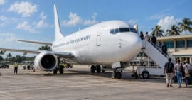Avión comercial estacionado en una plataforma aeroportuaria caribeña, con viajeros junto a una escalera de embarque.